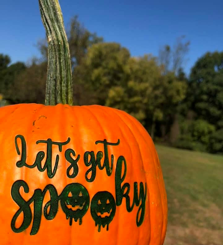 A pumpkin laser-engraved with the script words Let&rsquo;s get spooky, outdoors under a blue sky