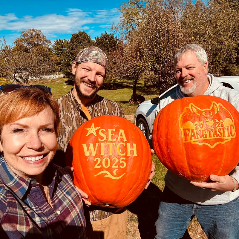 Three people outdoors holding two large pumpkins laser-engraved with Sea Witch 2025 and Fangtastic 2025