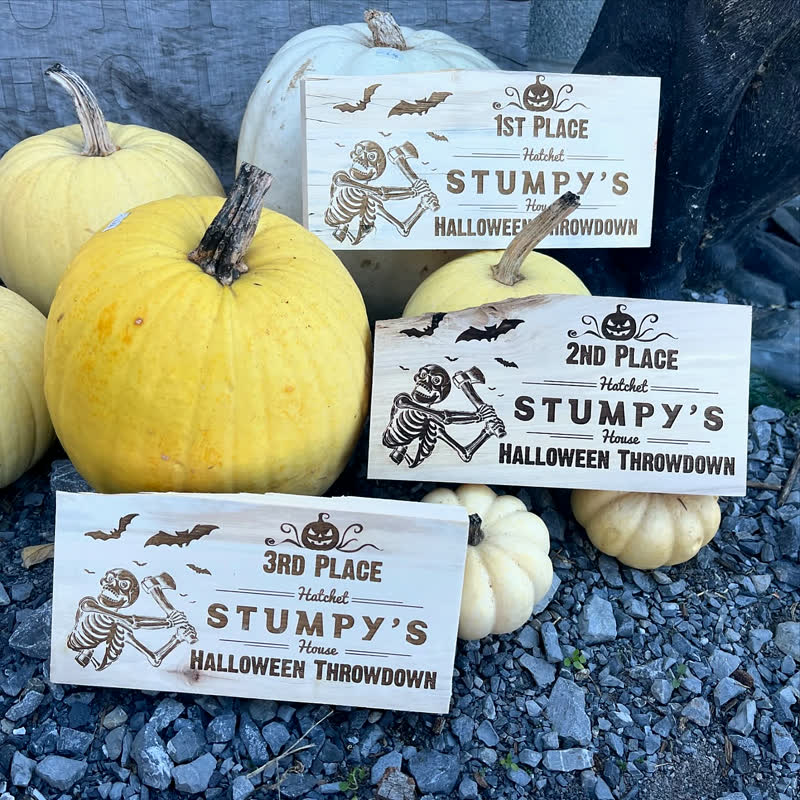 Three engraved wood award plaques for first, second, and third place at Stumpy&rsquo;s Halloween Throwdown, propped among white pumpkins