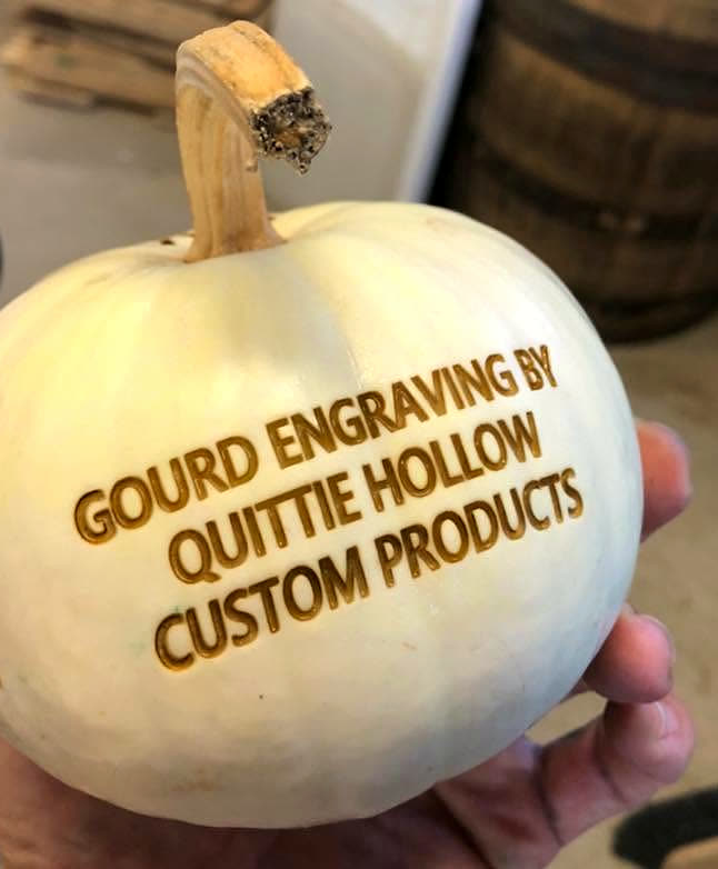 A small white gourd laser-engraved with the Quittie Hollow logo, held in a hand